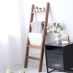 a wooden ladder leaning up against a wall next to a table with flowers on it