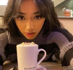 a woman is looking at the camera while holding a coffee cup with whipped cream on it