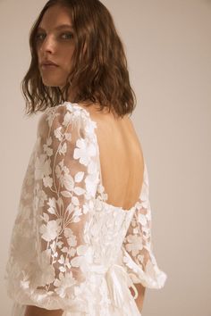 the back of a woman wearing a white wedding dress with sheer sleeves and floral appliques