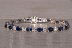 The Hingham: Natural Sapphire and Cluster Diamond Bracelet in White Gold. This exquisite bracelet showcases a series of stunning oval brilliant-cut natural sapphires, totaling 10.88 carats, elegantly set in an East to West orientation. Each sapphire is separated by a diamond flower section, adding a touch of sophistication and sparkle to the piece. The diamond sections feature a central round brilliant-cut natural diamond surrounded by six additional round brilliant-cut natural diamonds, with an Luxury Sapphire Diamond Bracelet With Gemstones, Luxury Sapphire And Diamond Bracelet, Luxury Sapphire Diamond Bracelet For Formal Events, Luxury Sapphire Diamond Bracelet For Formal Occasions, Luxury Sapphire Bracelet For Formal Occasions, Luxury Oval Diamond Bracelet With Gemstone, Elegant Sapphire Tennis Bracelet With Brilliant Cut, White Gold Sapphire Tennis Bracelet For Formal Occasions, Exquisite Oval Diamond Bracelet For Formal Occasions