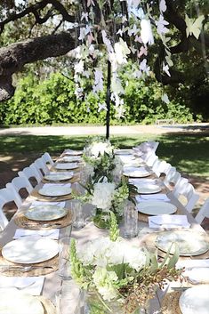 an outdoor table set with plates and place settings for dinner under the shade of a tree