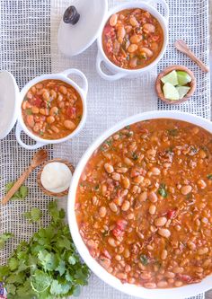 three bowls of beans and cilantro on a table with spoons next to them