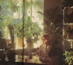 a woman sitting at a table in front of a potted plant next to a window