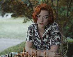 a woman sitting at a table with a chess board and pieces in front of her