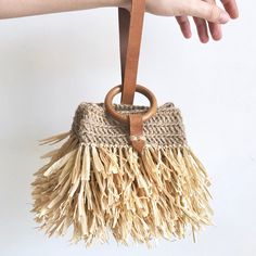 a hand holding a straw purse with wooden handles