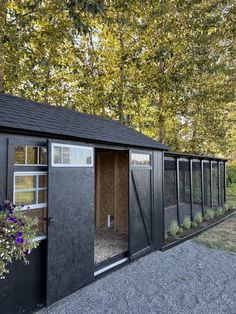 a small black shed with windows and doors on the outside, in front of some trees