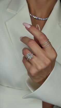 a woman in a white suit holding a diamond ring on her left hand and wearing a pink manicure