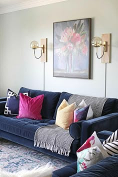 a living room with blue couches and colorful pillows on the sofa, along with two sconces