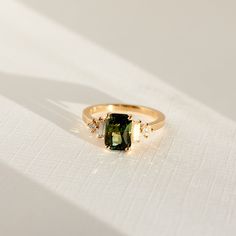 a gold ring with a green stone surrounded by small white diamonds on a plain surface