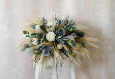 an arrangement of flowers and foliage on a white stool against a wall with a beige background