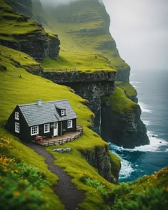 a small house on the side of a cliff by the ocean with cliffs in the background