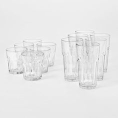 six clear glass tumblers lined up on a white surface with no one in them