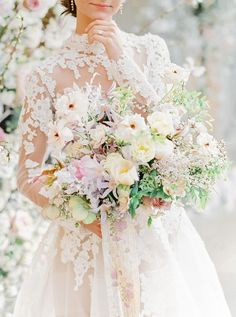 a woman in a wedding dress holding a bouquet of white and pink flowers with her hand on her chin