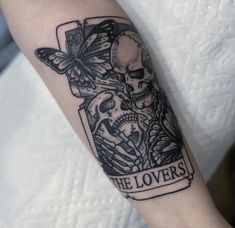 a black and white photo of a skull with butterflies on it's arm that says the lovers