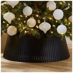 a christmas tree with white ornaments and lights on it's branches in a black pot