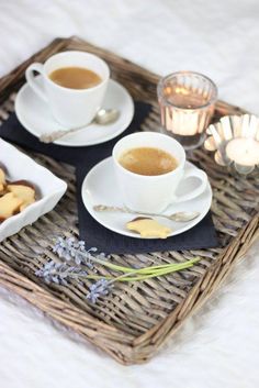 two cups of coffee are sitting on a tray with cookies and lavender sprigs