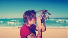 a man on the beach looking at an old boat wheel in front of his face