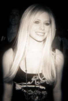 a woman with long blonde hair wearing a black top and smiling at the camera while standing next to other people