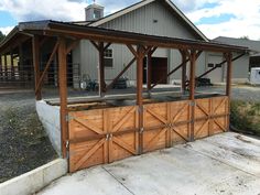 a wooden garage with two doors open in front of a barn and horse pens on the other side