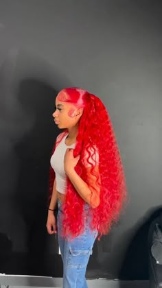 a woman with long red hair standing in front of a black wall and wearing jeans