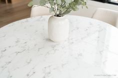 a white vase filled with flowers sitting on top of a marble dining room table in front of a window