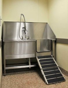 a stainless steel sink in the corner of a room with stairs leading up to it