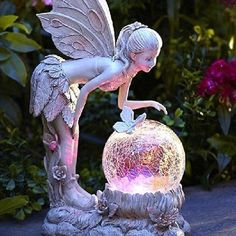 a fairy figurine sitting on top of a ball in the middle of flowers