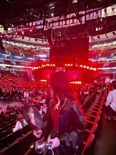 a woman standing in front of an audience at a concert with red lights on the stage