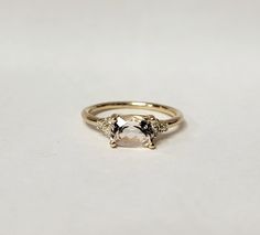 a gold ring with an oval stone and two smaller stones on the side, sitting on a white surface