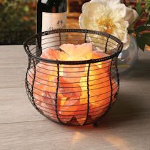 a wine bottle and some fruit in a wire basket on a wooden table with flowers