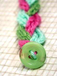 a green button sitting on top of a table next to a piece of string and yarn