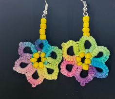 multicolored crochet earrings with beads hanging from hooks on black background, closeup