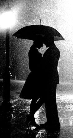 black and white photograph of two people kissing under an umbrella in the rain at night