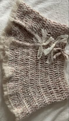 two pieces of knitted clothing laying on top of a white bed sheet with fraying around the edges