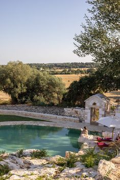 an outdoor swimming pool surrounded by rocks and greenery in the middle of a field