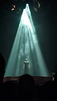 a person standing in the middle of a stage with light coming from behind them and people watching