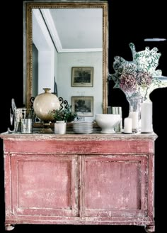 an old dresser with plates and vases on it in front of a large mirror