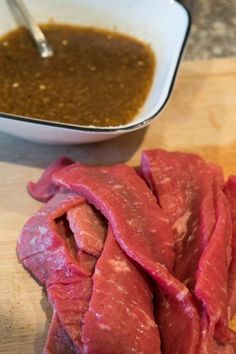 some raw meat is sitting on a cutting board next to a bowl of gravy