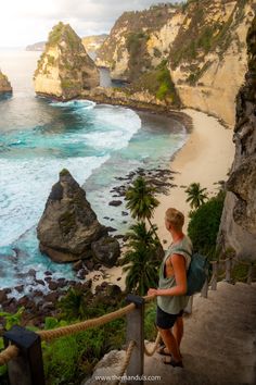 a woman walking up some steps to the beach next to rocks and water with palm trees on either side