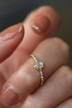 a close up of a person's hand holding a gold ring with an opal stone