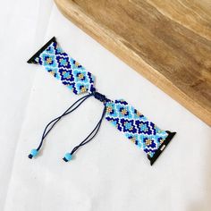 a blue and yellow beaded bracelet sitting on top of a wooden board next to a piece of wood