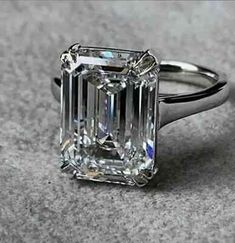 an emerald - cut diamond ring sits on a gray surface