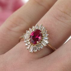 a close up of a person's hand holding a ring with a red stone