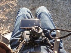 a person sitting on the ground with a camera and cell phone in their lap top