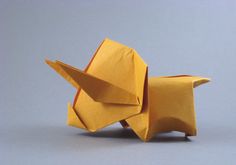 an origami dog made out of yellow paper on a gray surface with the tail folded up