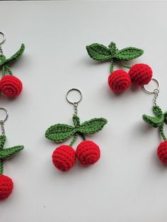 four crocheted cherries with leaves on them hanging from keychain hooks