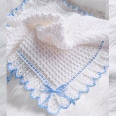 a white crocheted blanket with blue trim on it and a baby's hat