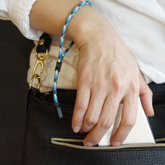 a woman's hand holding onto a black purse with a blue and white beaded bracelet on it