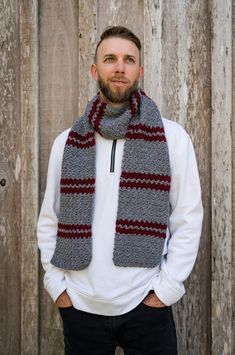 a man standing in front of a wooden fence wearing a gray and red knitted scarf