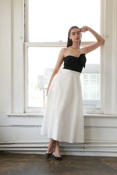 a woman standing in front of a window wearing a black and white dress